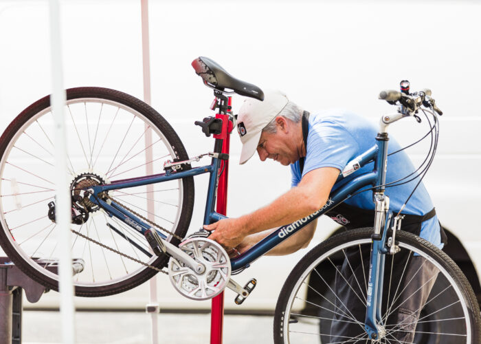 A man working on a bicycle in front of a red pole.