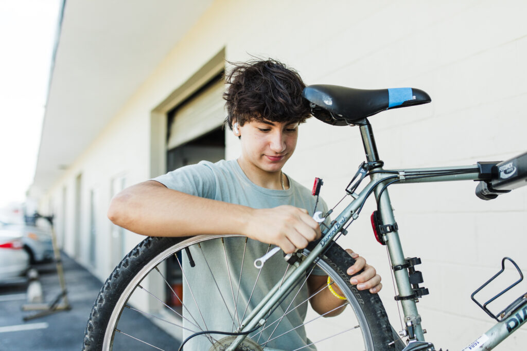 A boy is fixing his bike outside of the house.